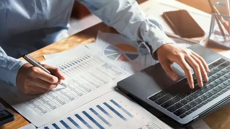 An accountant annotating printed financial statements beside a laptop.