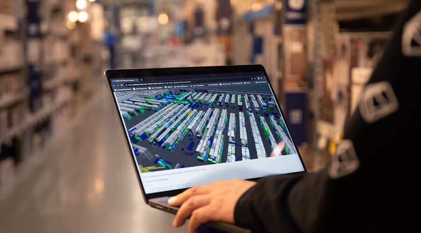A laptop held in a warehouse aisle, showing a mapped view of the racking